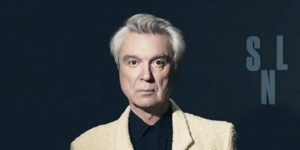 David Byrne performs ‘Once in a Lifetime’ and ‘Toe Jam’ on SNL, joins ‘Airport Sushi’ sketch